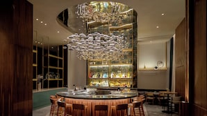 Uma área de bar com balcão arredondado, cadeiras de madeira e um lustre decorativo.