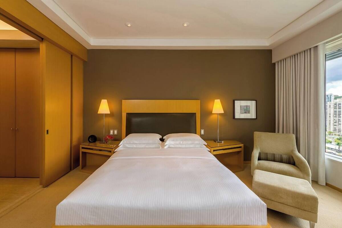 Una habitación de hotel con una cama grande, dos lámparas de noche, una silla y una ventana con cortinas.