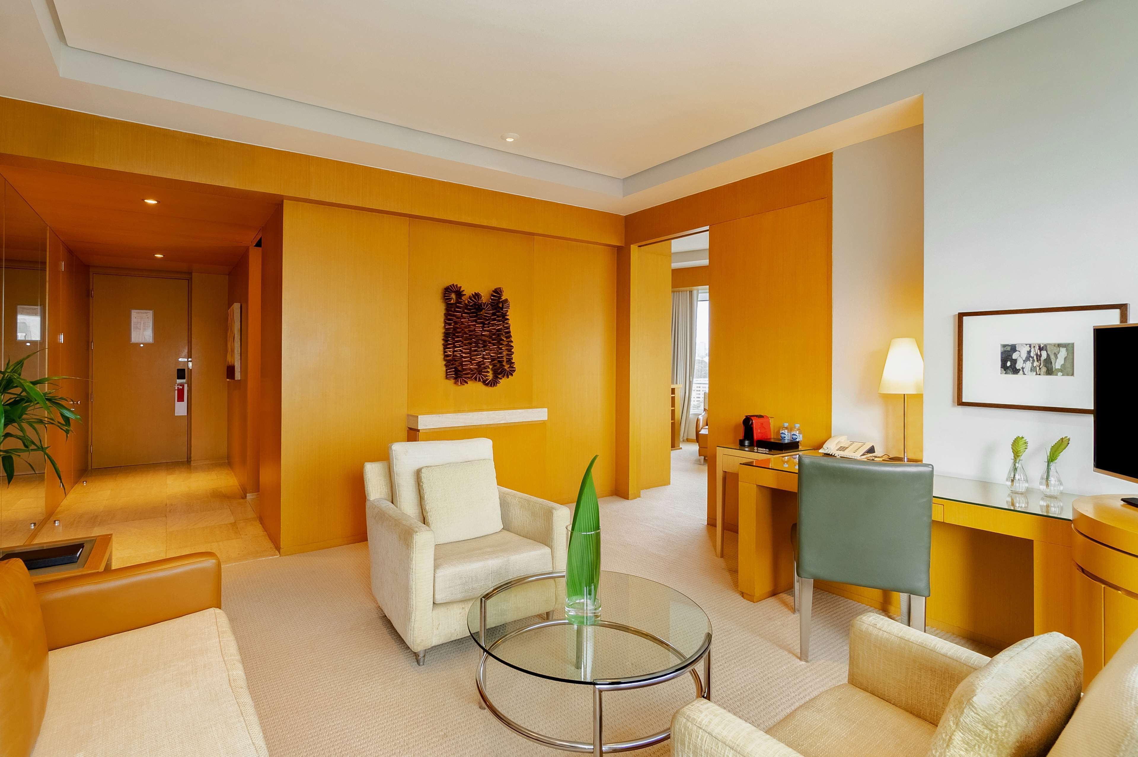 A hotel lobby with a modern design, featuring a glass coffee table, a sofa, a desk, and a chair.