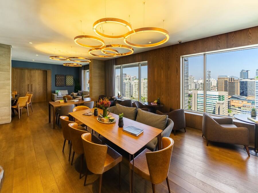 Un espace de repas moderne avec une table et des chaises en bois, un canapé et une grande fenêtre donnant sur la ville.