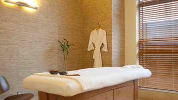 Relax in a serene spa room with a massage table, comfortable chair, and soothing greenery.