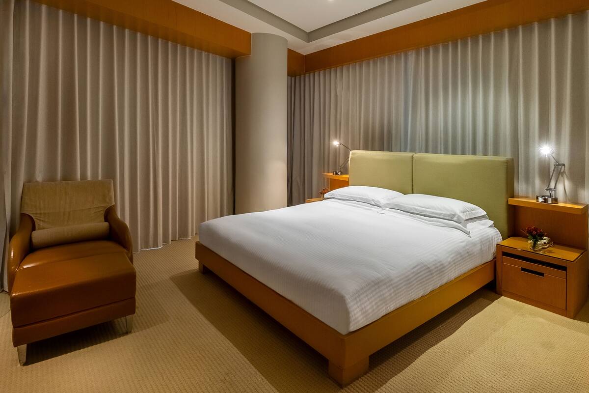Una habitación de hotel con una cama grande, una silla, una mesita de noche y una lámpara.