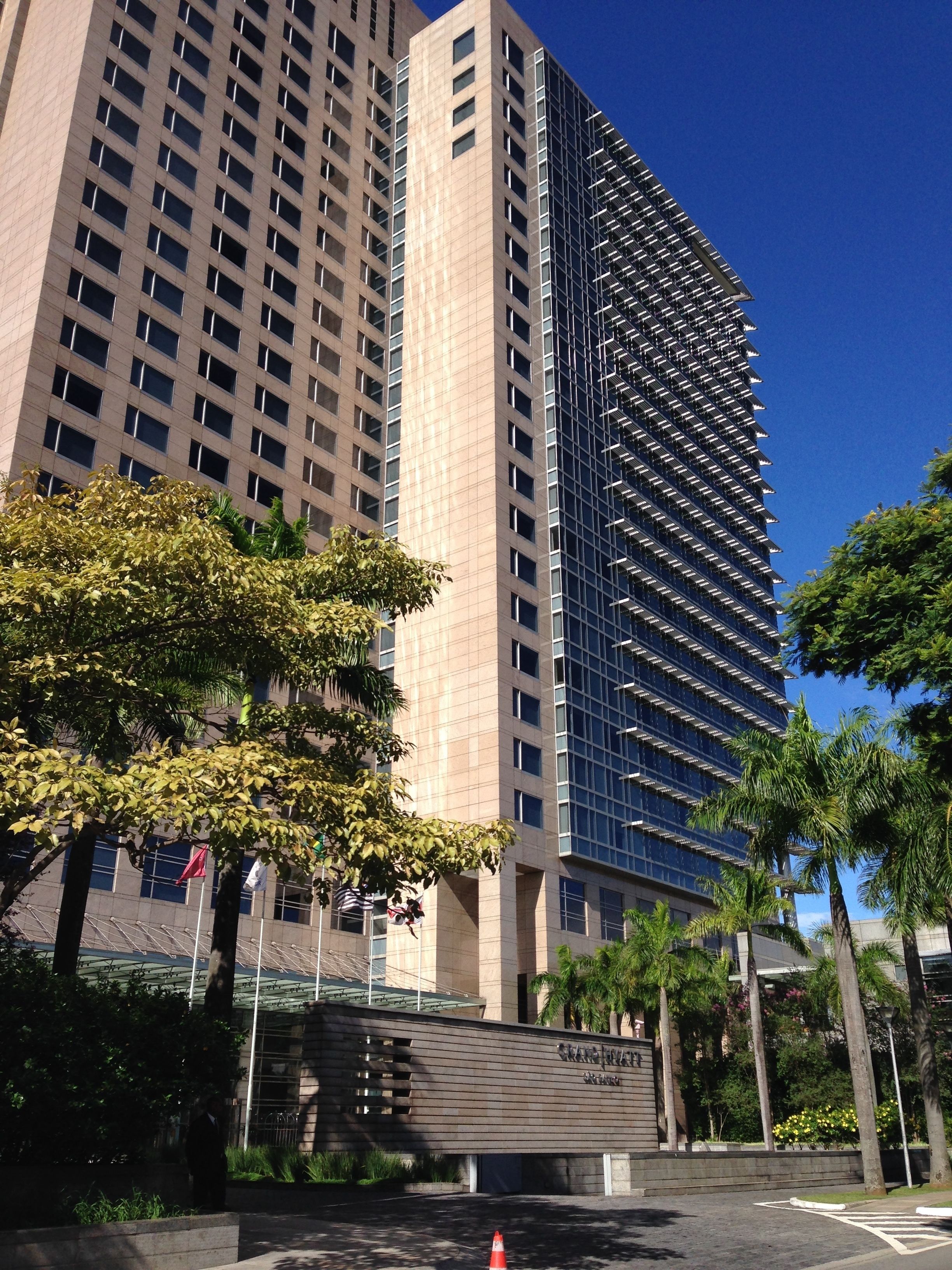 A high-rise building with a modern glass facade, surrounded by palm trees and a well-maintained landscaped area.