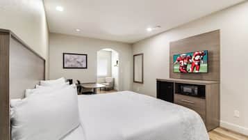 A hotel room with a large bed, a television mounted on the wall, a small desk, and a microwave.