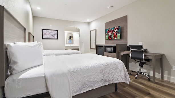 A hotel room with a large bed, a desk with a computer, a television, and a mirror. - Red Roof Inn PLUS+ Galveston - Beachfront (Galveston)