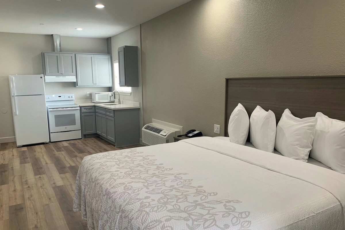 A hotel room with a bed, a kitchenette, and a bathroom.