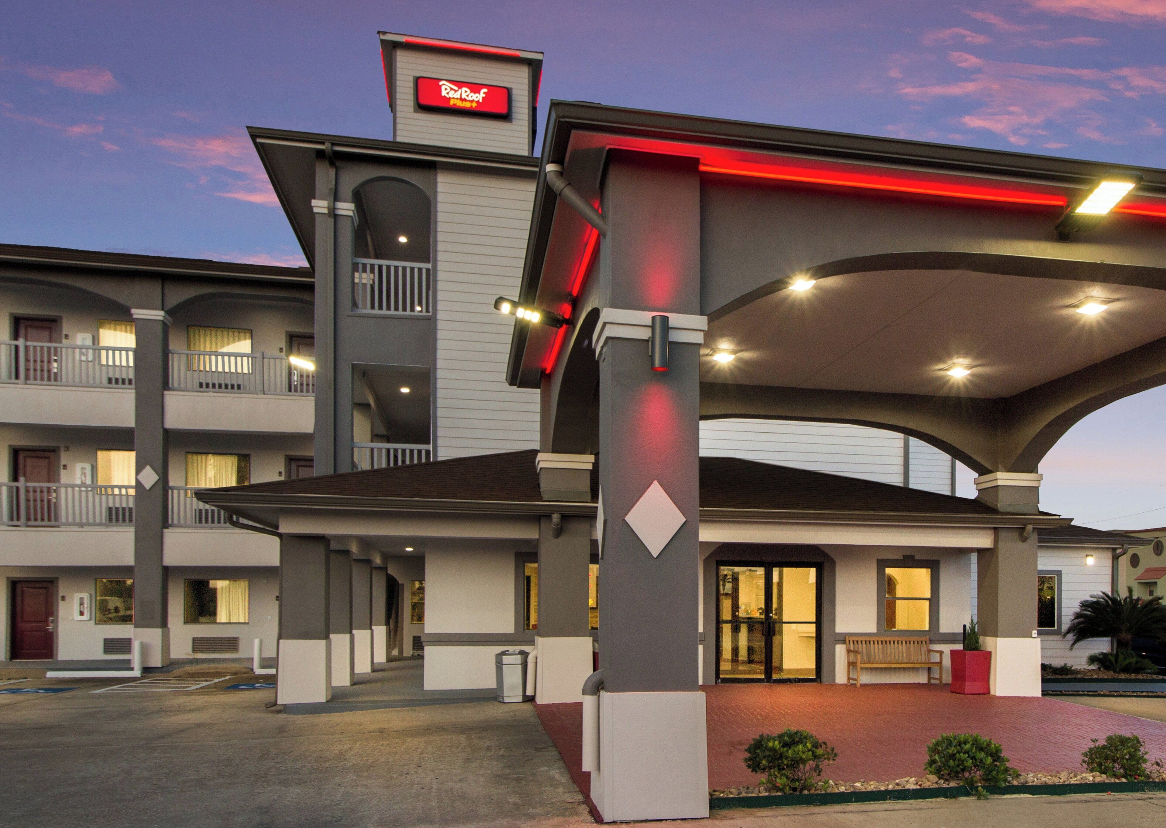 Un motel con entrada central, zona de estacionamiento techada y un cartel con el nombre.