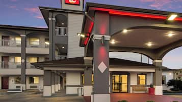 Un motel con entrada central, zona de estacionamiento techada y un cartel con el nombre.