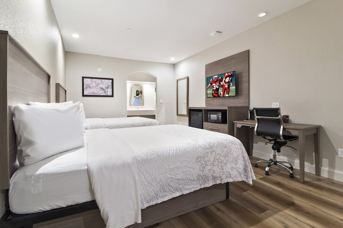 Una habitación de hotel con una cama grande, un escritorio con computadora, un televisor y un espejo.