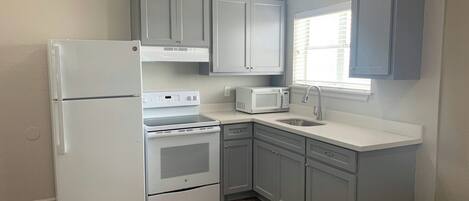 A compact kitchen with a refrigerator, stove, microwave, and sink.
