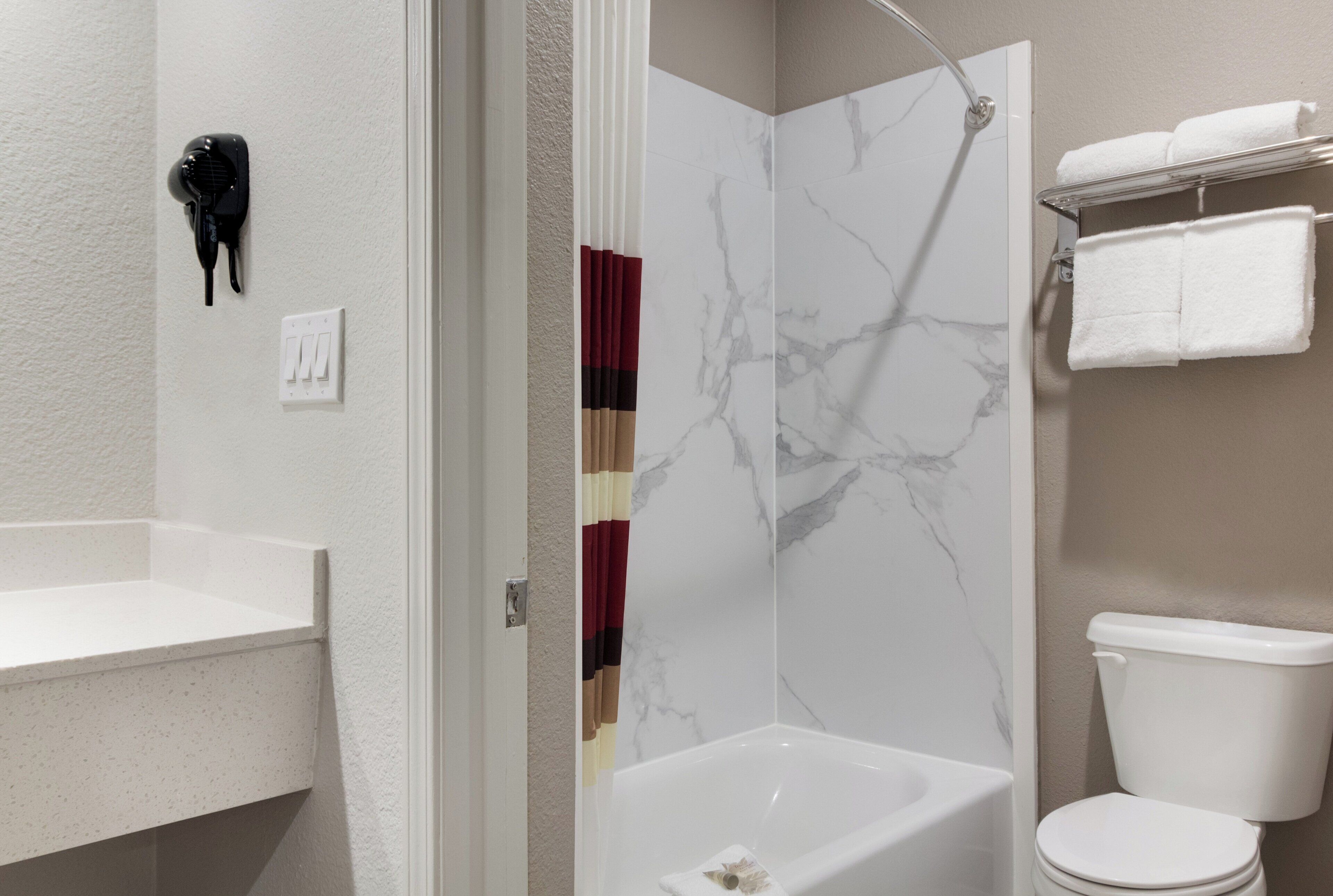 A bathroom with a white bathtub, a toilet, and a shower area with a marble wall.