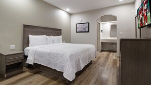 Un dormitorio con una cama grande, una mesita de noche, un aparador, un espejo y un televisor montado en la pared.