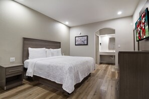 A bedroom with a large bed, a nightstand, a dresser, a mirror, and a TV mounted on the wall.
