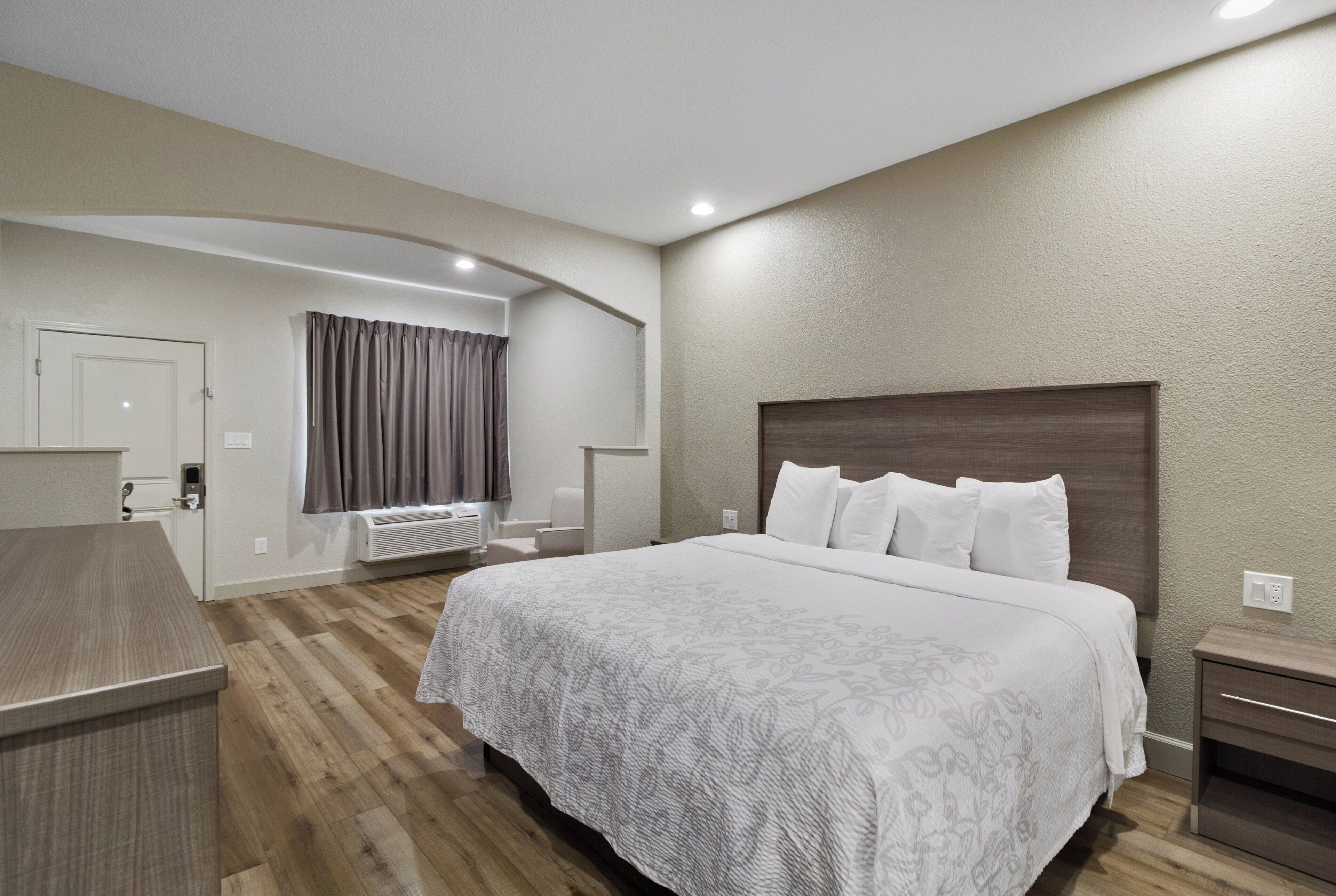 Habitación de hotel con una cama grande, un escritorio, una silla y un ventanal con cortinas.