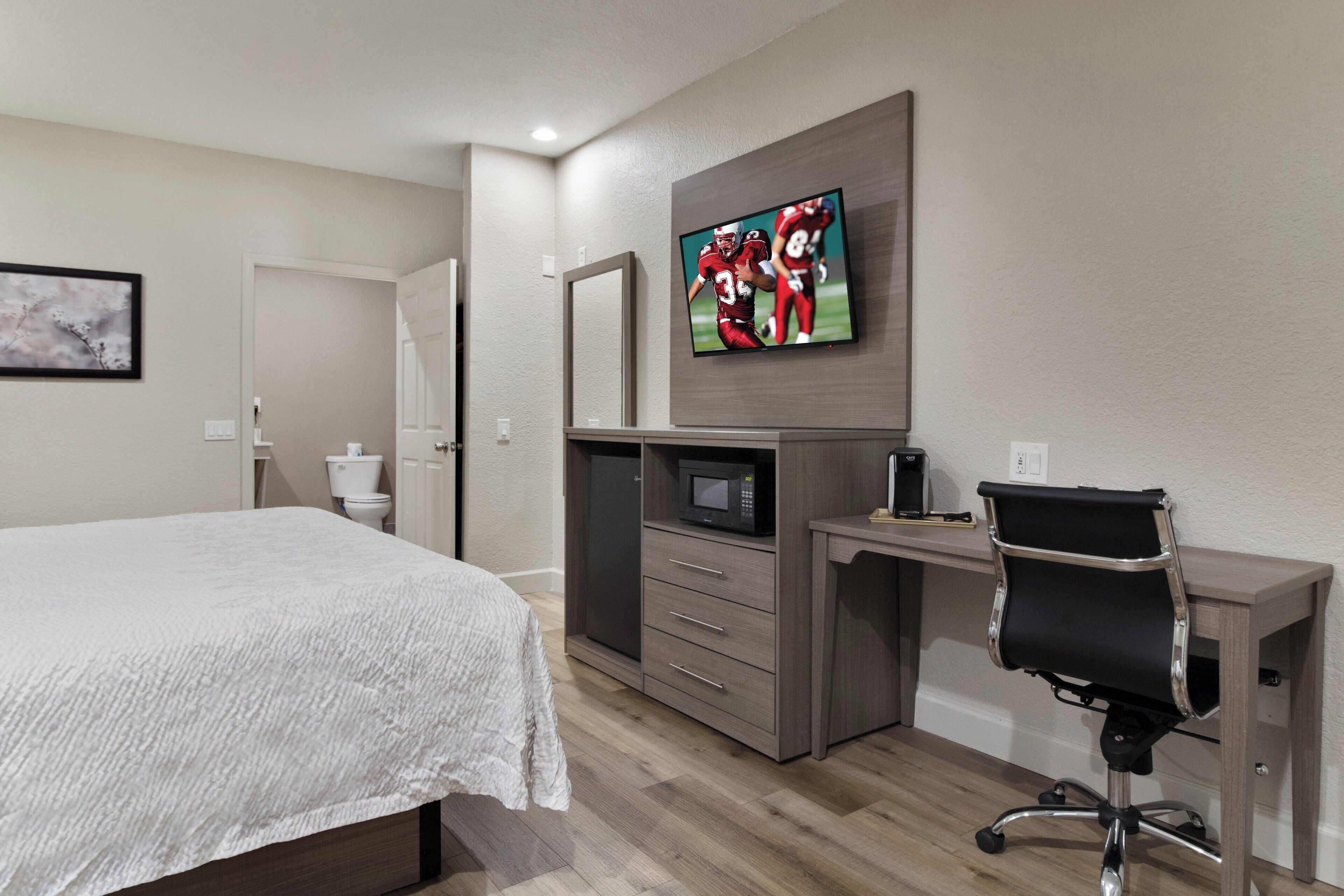 Une chambre d’hôtel équipée d’un lit, d’un bureau avec une chaise, d’une télévision, d’un four à micro-ondes et d’une machine à café.