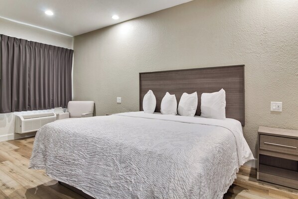 A modern hotel room with a large bed, a bedside table, a chair, and a built-in heater. - Red Roof Inn PLUS+ Galveston - Beachfront (Galveston)