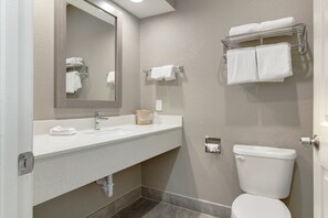 A bathroom with a white sink, mirror, and toilet. There are towels on a rack and a soap dispenser on the sink.