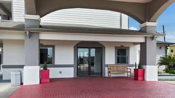 A building entrance with a covered walkway, a bench, and potted plants.