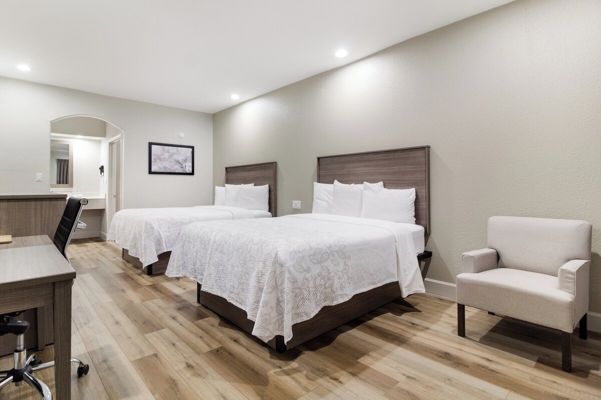 A hotel room with two beds, a desk, a chair, and a mirror.