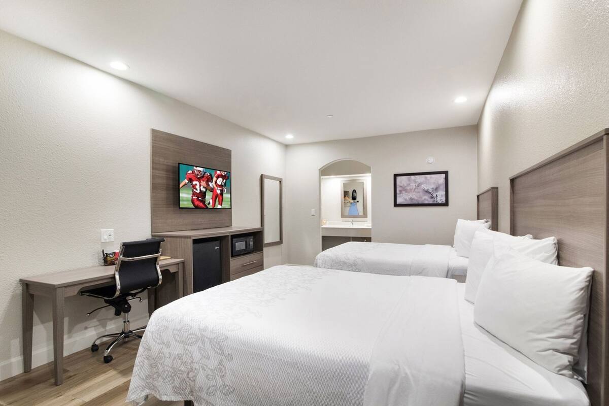 Habitación de hotel con dos camas, un escritorio con silla, televisor, microondas y refrigerador pequeño.