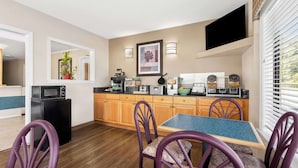A compact kitchen with wooden cabinets, a microwave, and a dining area with purple chairs. - Econo Lodge St. George (St. George)