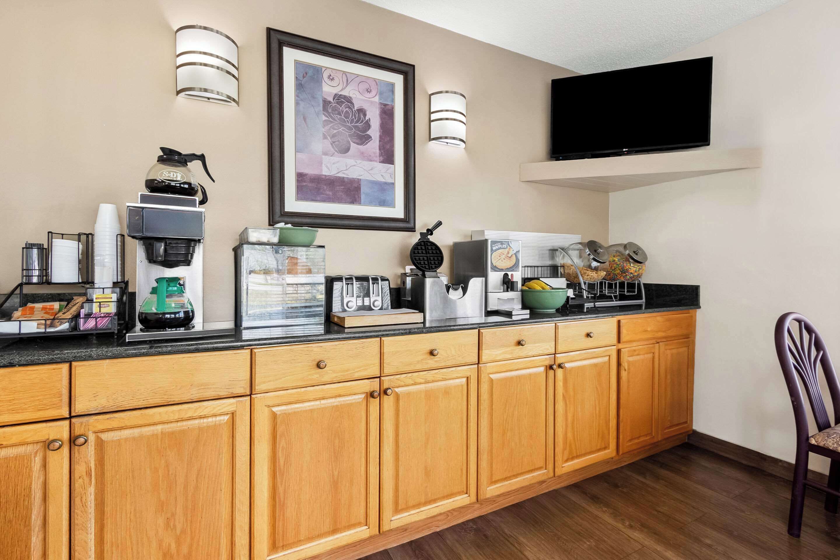 A kitchen with wooden cabinets, a coffee machine, a waffle maker, and a TV mounted on the wall.