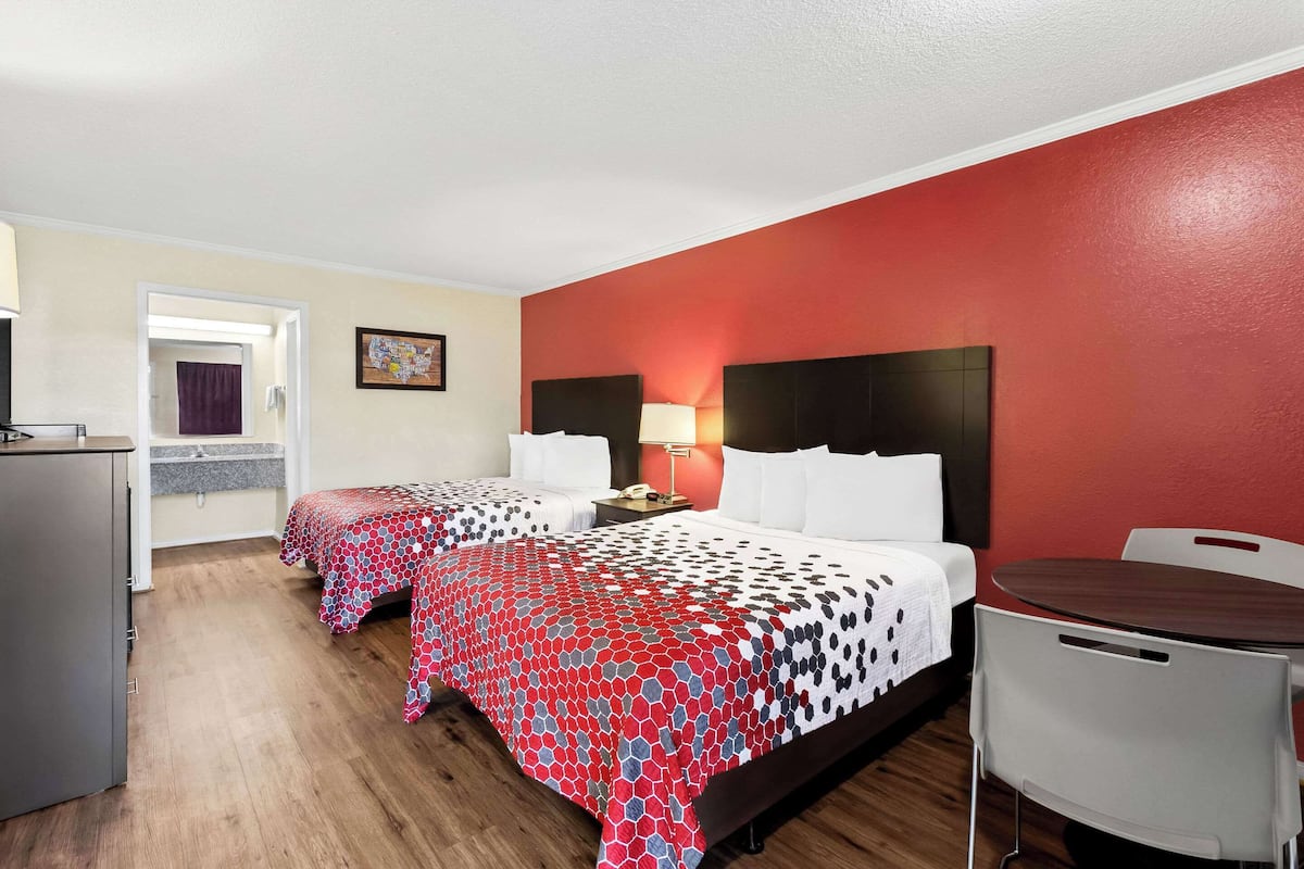 Quarto de hotel com duas camas, uma escrivaninha, uma cadeira e uma mesa.