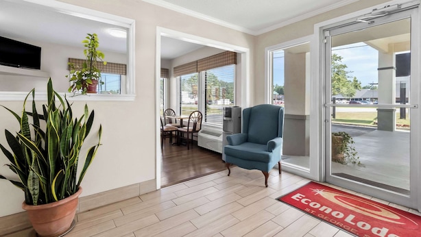 A hotel lobby with a large potted plant, a blue armchair, a dining area with chairs and a table, and a red doormat with the hotel name. - Econo Lodge St. George (St. George)