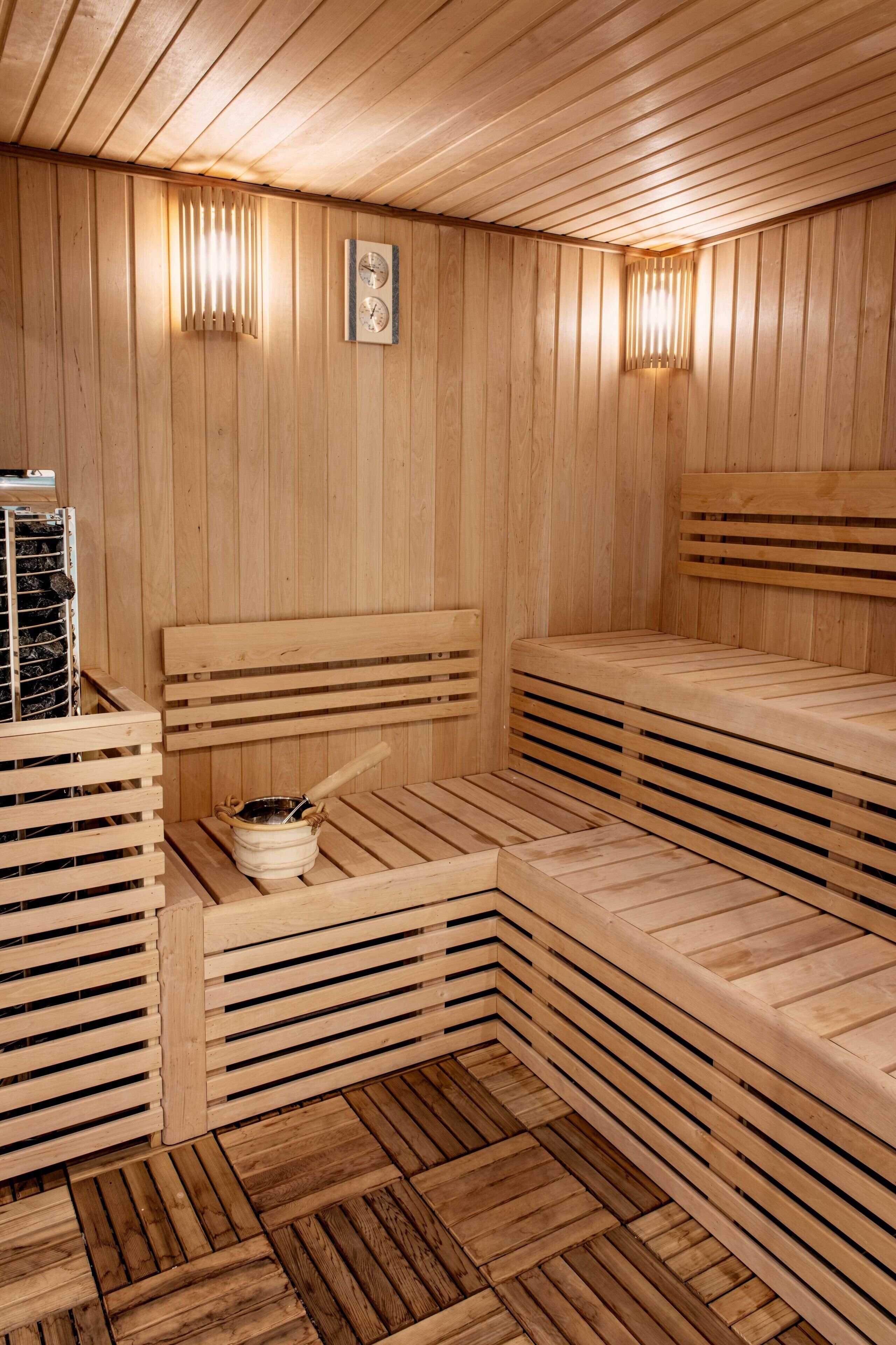 Un sauna avec des bancs en bois, un thermomètre fixé au mur et un appareil de chauffage.