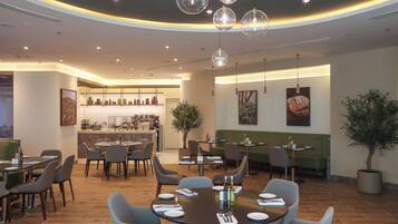 A modern restaurant with round tables, chairs, and a bar area.