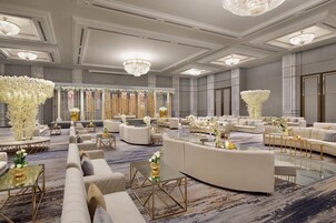 Uma área de estar ampla e elegantemente decorada, com assentos confortáveis, arranjos florais decorativos e iluminação suave.