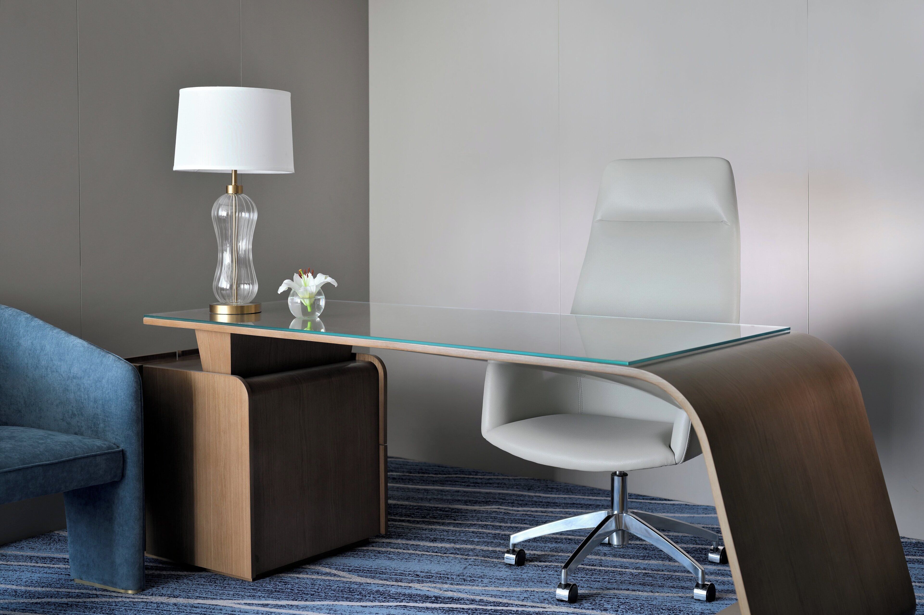 Un bureau moderne avec un plateau en verre, une chaise blanche, un canapé bleu et une lampe avec un abat-jour blanc.