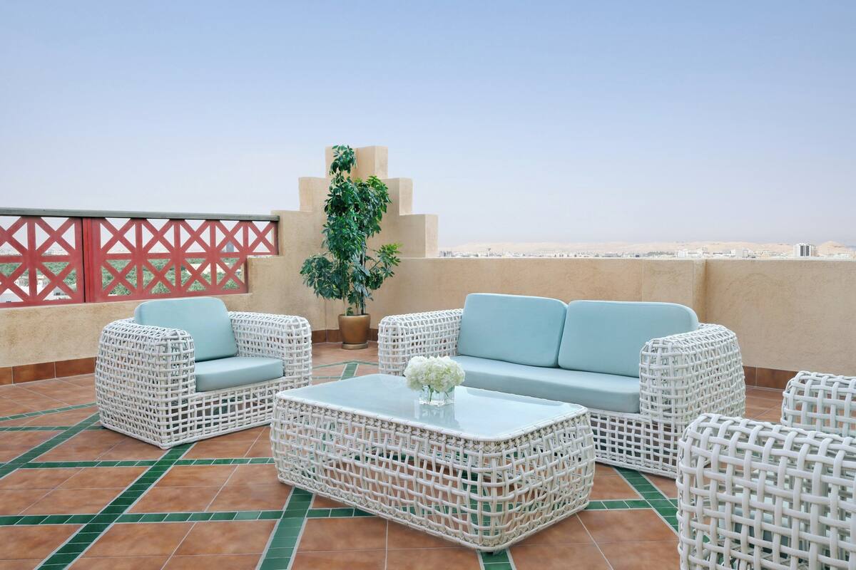 Una terraza en la azotea con mobiliario de mimbre, una planta en maceta y vistas de la ciudad.