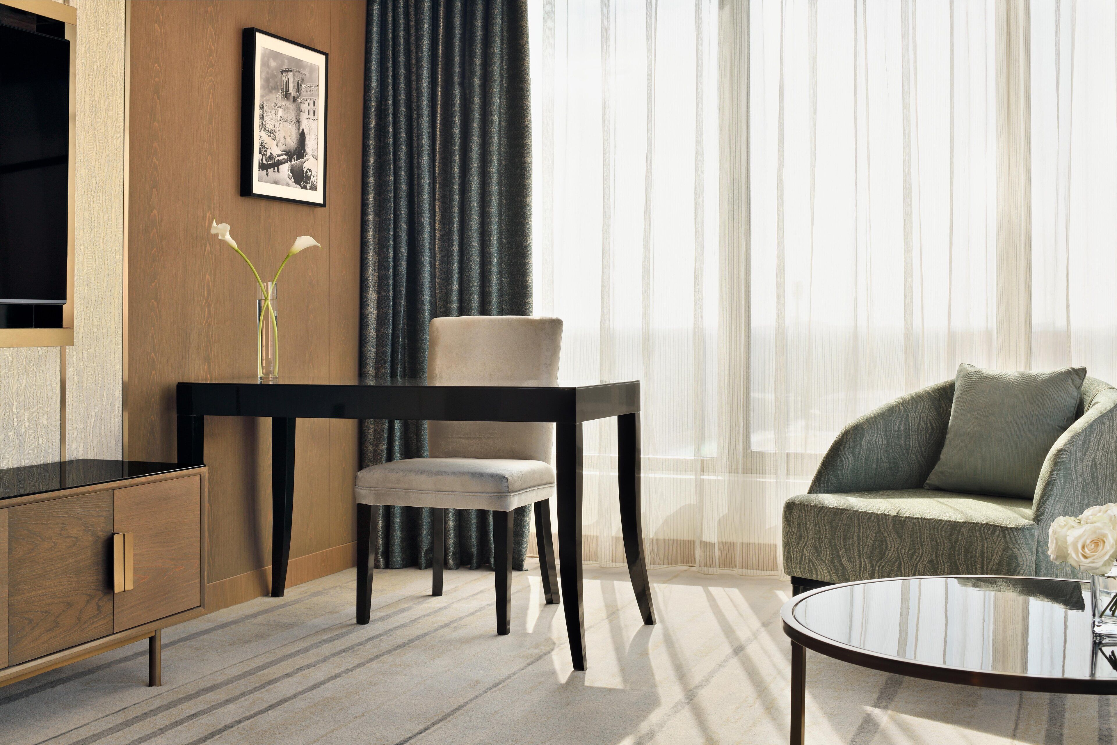 A modern hotel room with a wooden cabinet, a dining table with a chair, a sofa, and a glass coffee table.