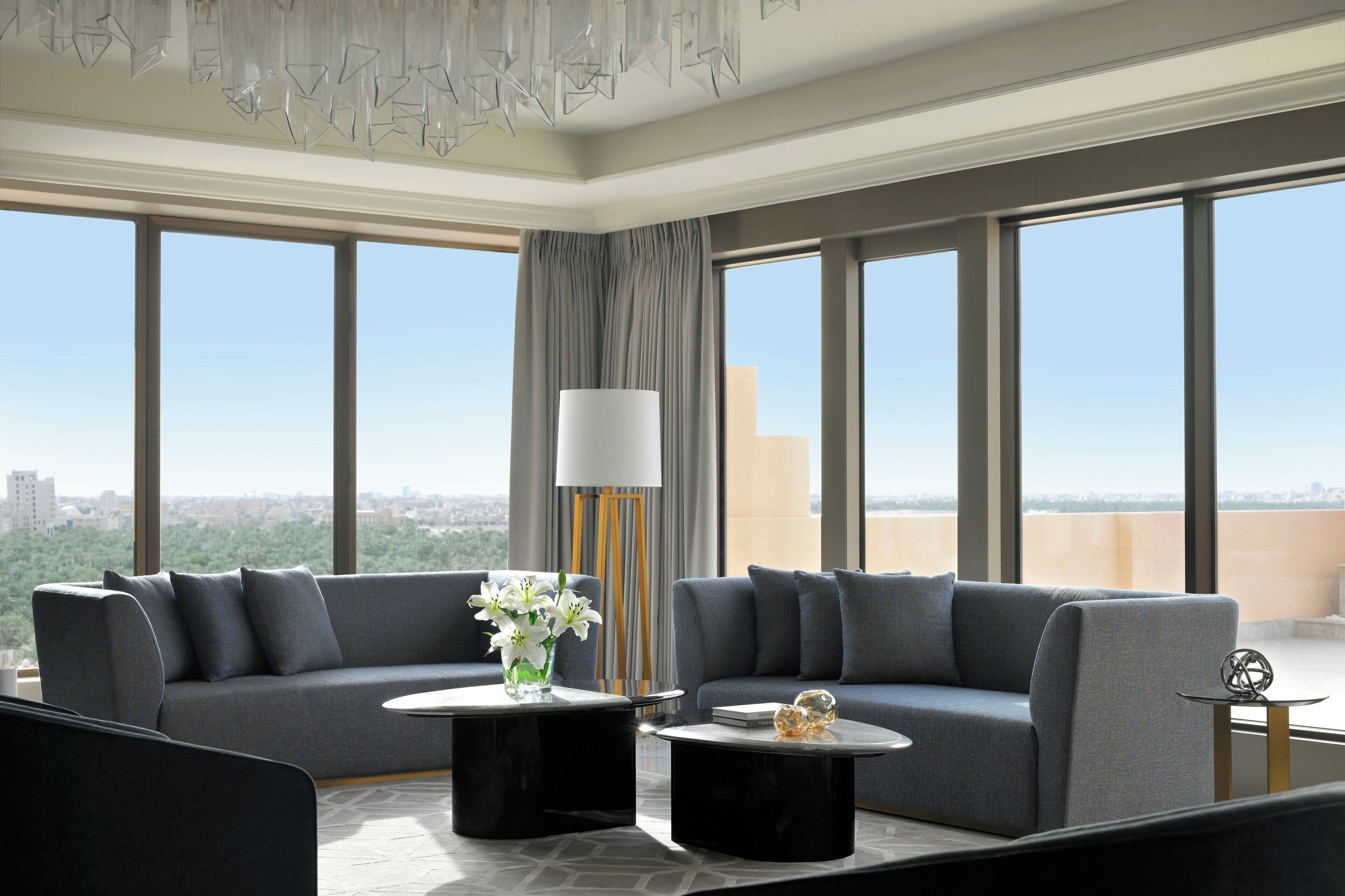 A modern living room with a grey sofa, two black coffee tables, a floor lamp, and a view of the city.