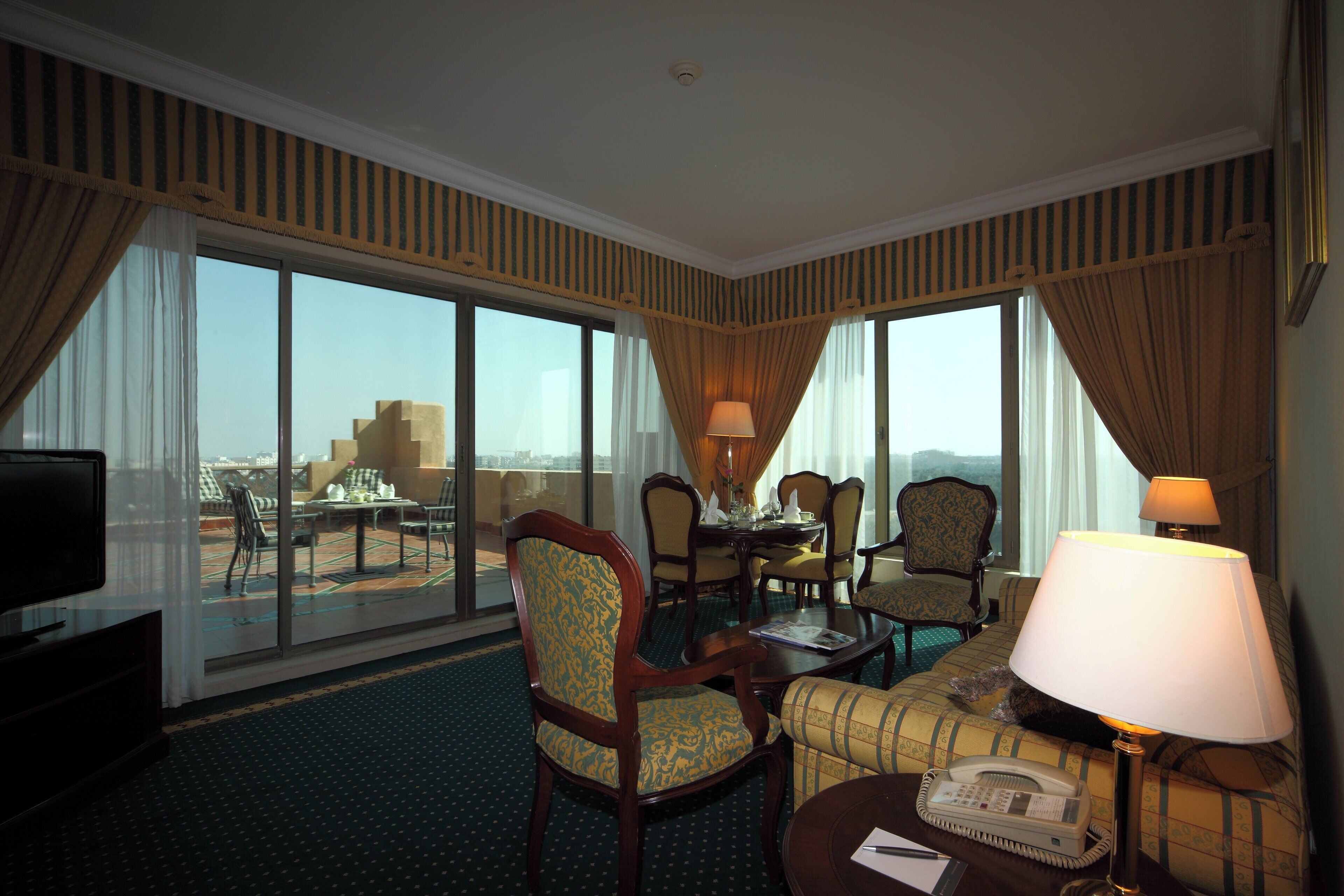 Una habitación de hotel con balcón, zona de comedor y sala de estar con sofá y sillones.