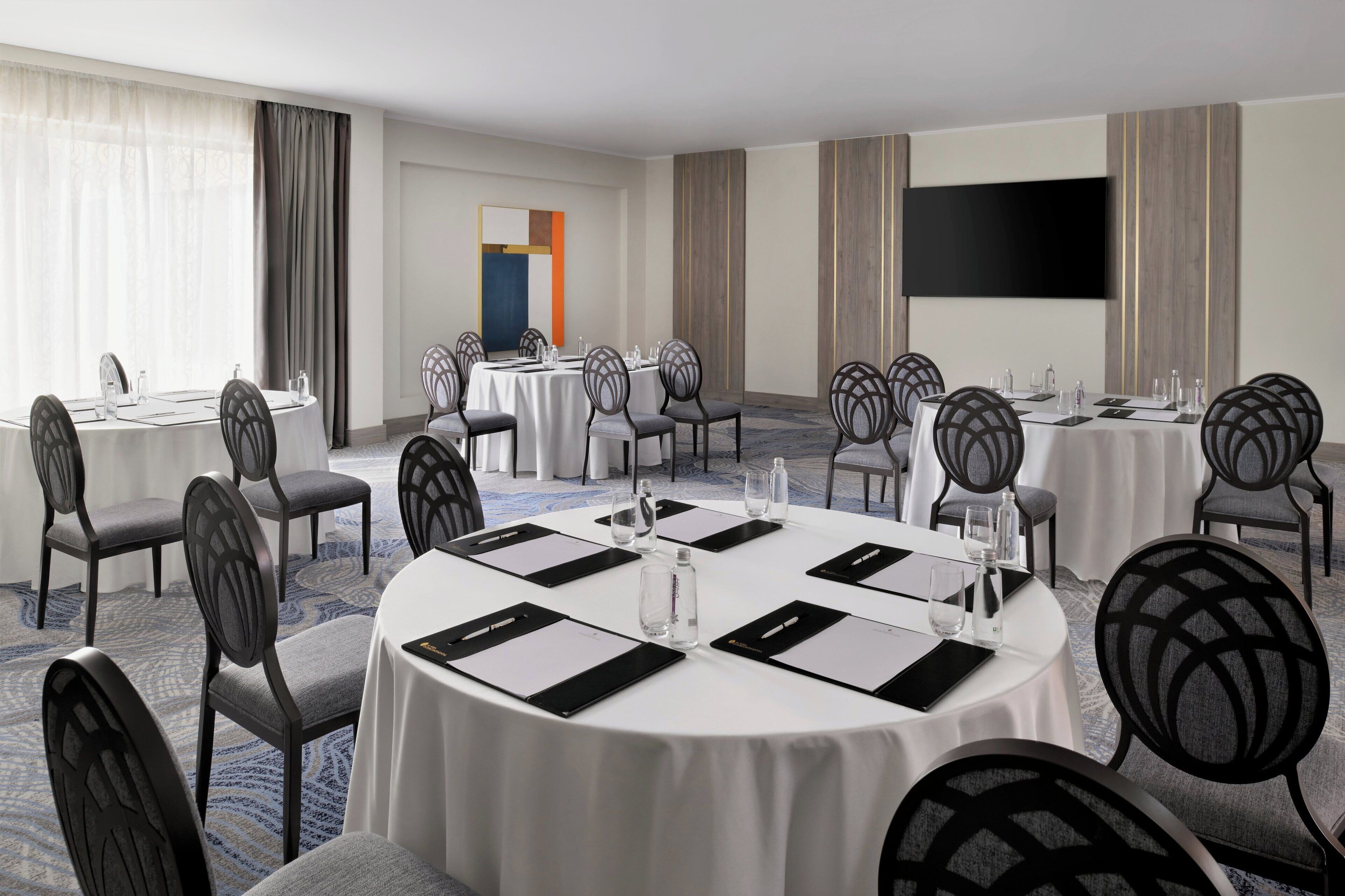 A conference room with round tables, chairs, and a large flat-screen TV.