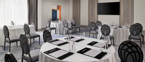A conference room with round tables, chairs, and a large flat-screen TV.