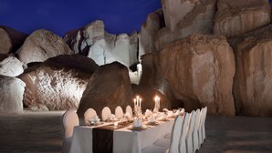 A formal dining table set for a meal in a desert environment with large rock formations in the background. - Al Ahsa InterContinental by IHG (Al-Hofuf)