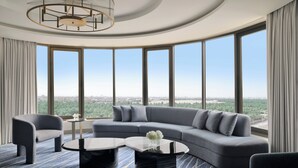 A modern living room with a curved sectional sofa, two round coffee tables, and a large window offering a city view. - Al Ahsa InterContinental by IHG (Al-Hofuf)