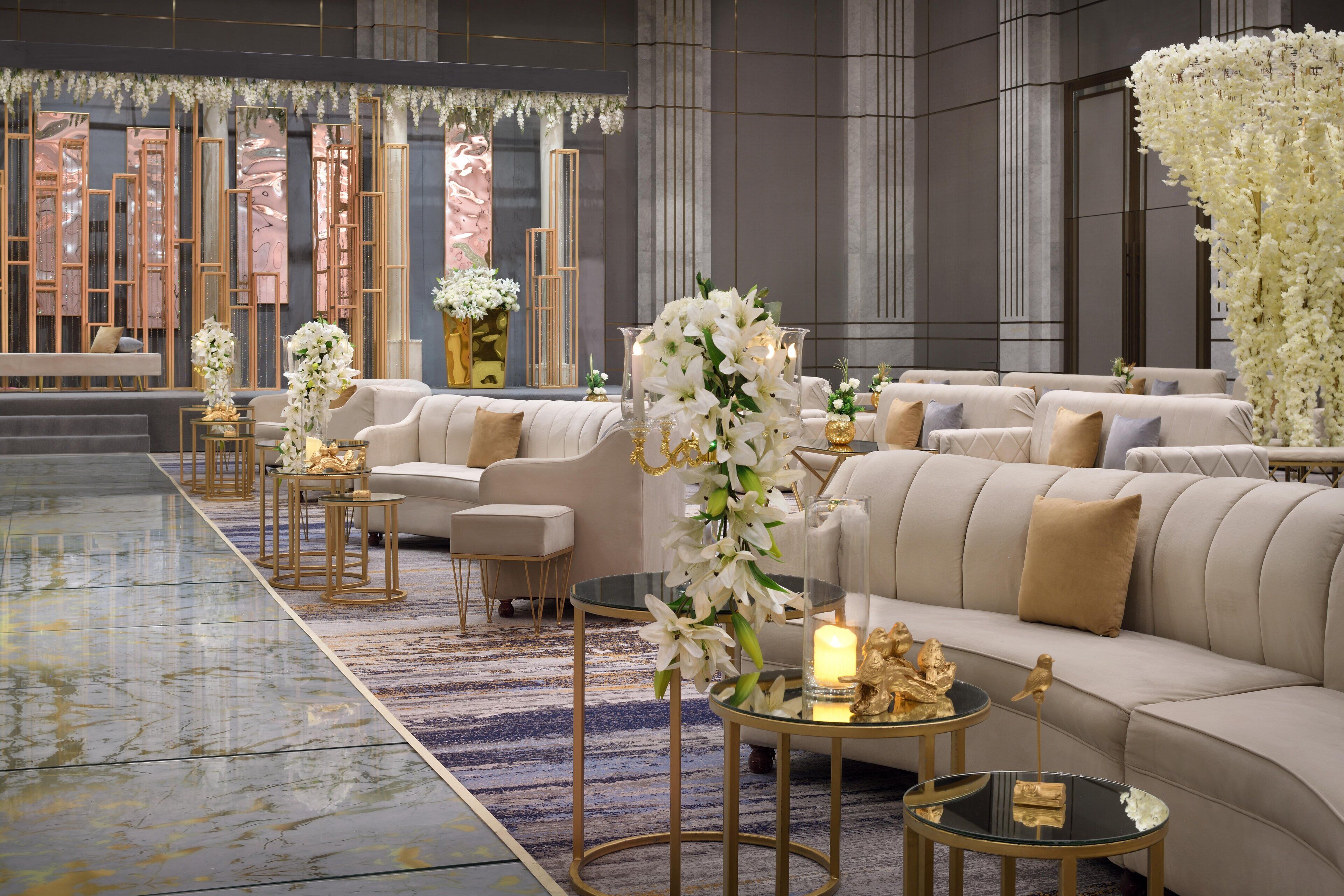 A luxurious lobby with a marble floor, plush sofas, and elegant decor including white flowers and gold accents.