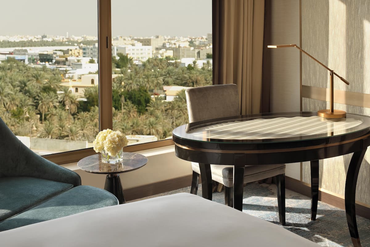 Habitación de hotel con vistas a un paisaje urbano, una mesa redonda, una silla y una lámpara.