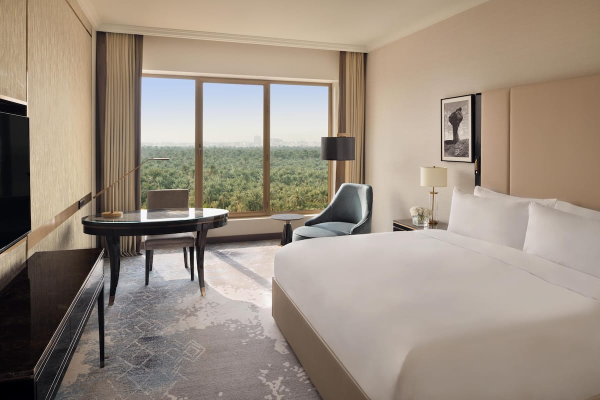 Habitación de hotel con una cama grande, un escritorio con silla, una mesita, un televisor y una ventana con vista a la ciudad.