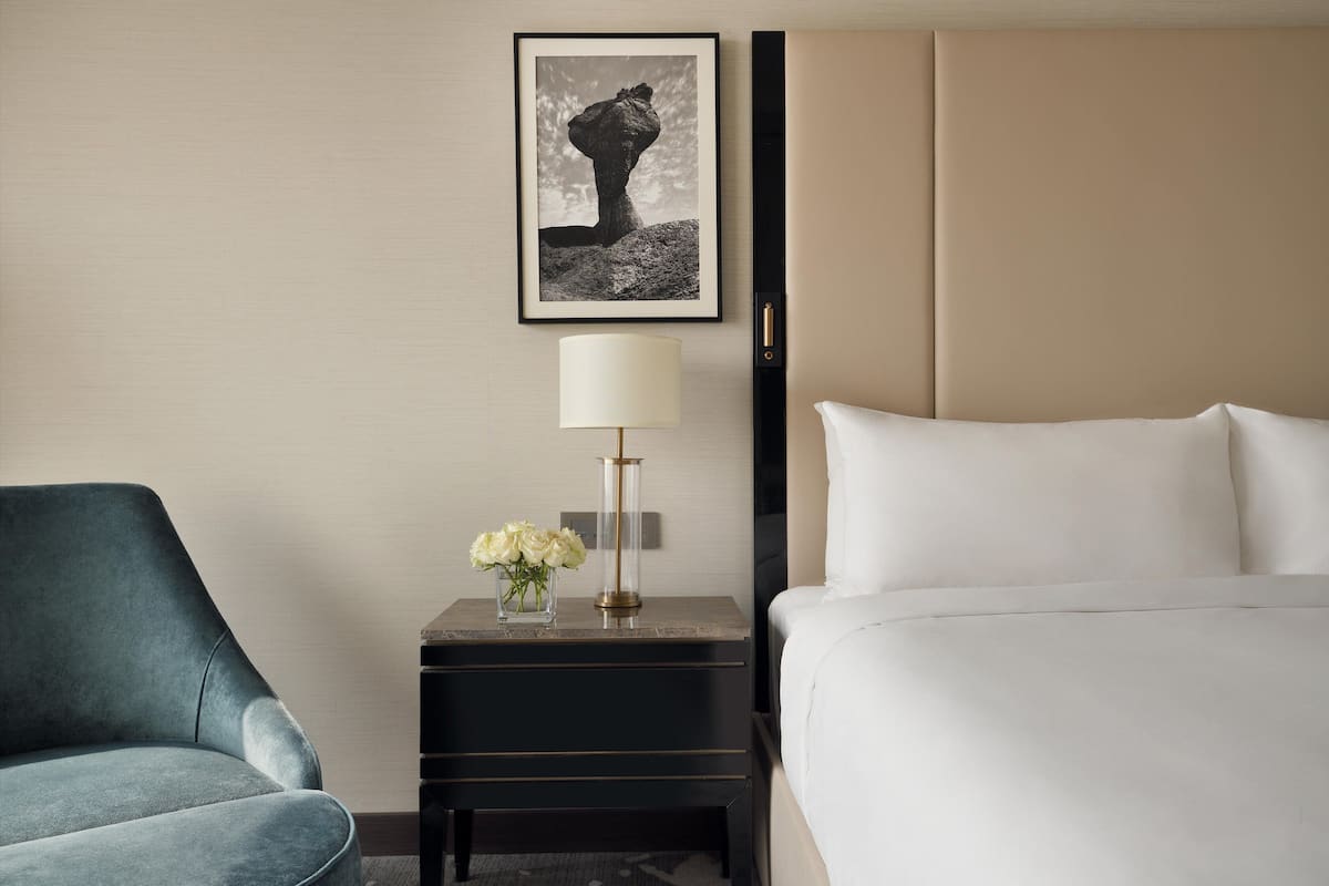 Una habitación de hotel con una cama, una mesita de noche con una lámpara y flores, y una silla.