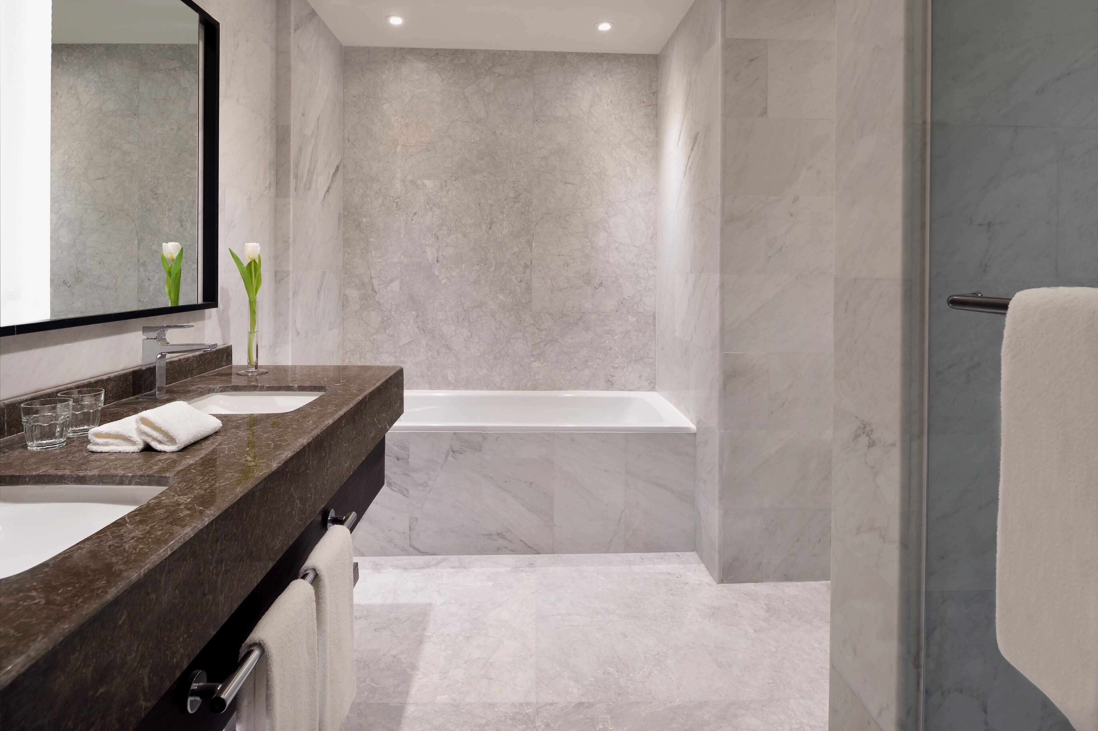 A modern bathroom with two sinks, a bathtub, and a large mirror.