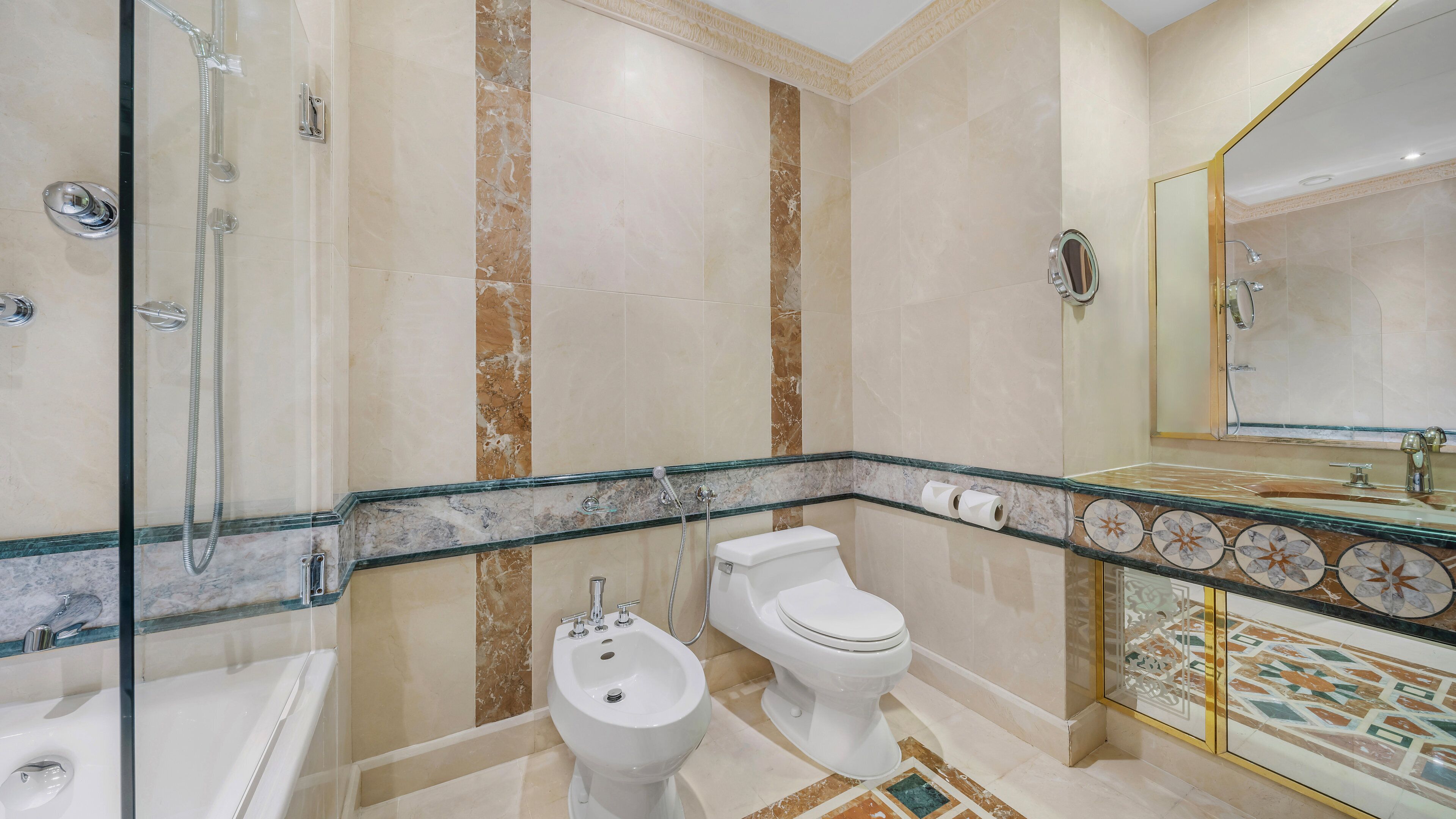 A bathroom with a glass-enclosed shower, a bidet, a toilet, and a sink with a mirror.
