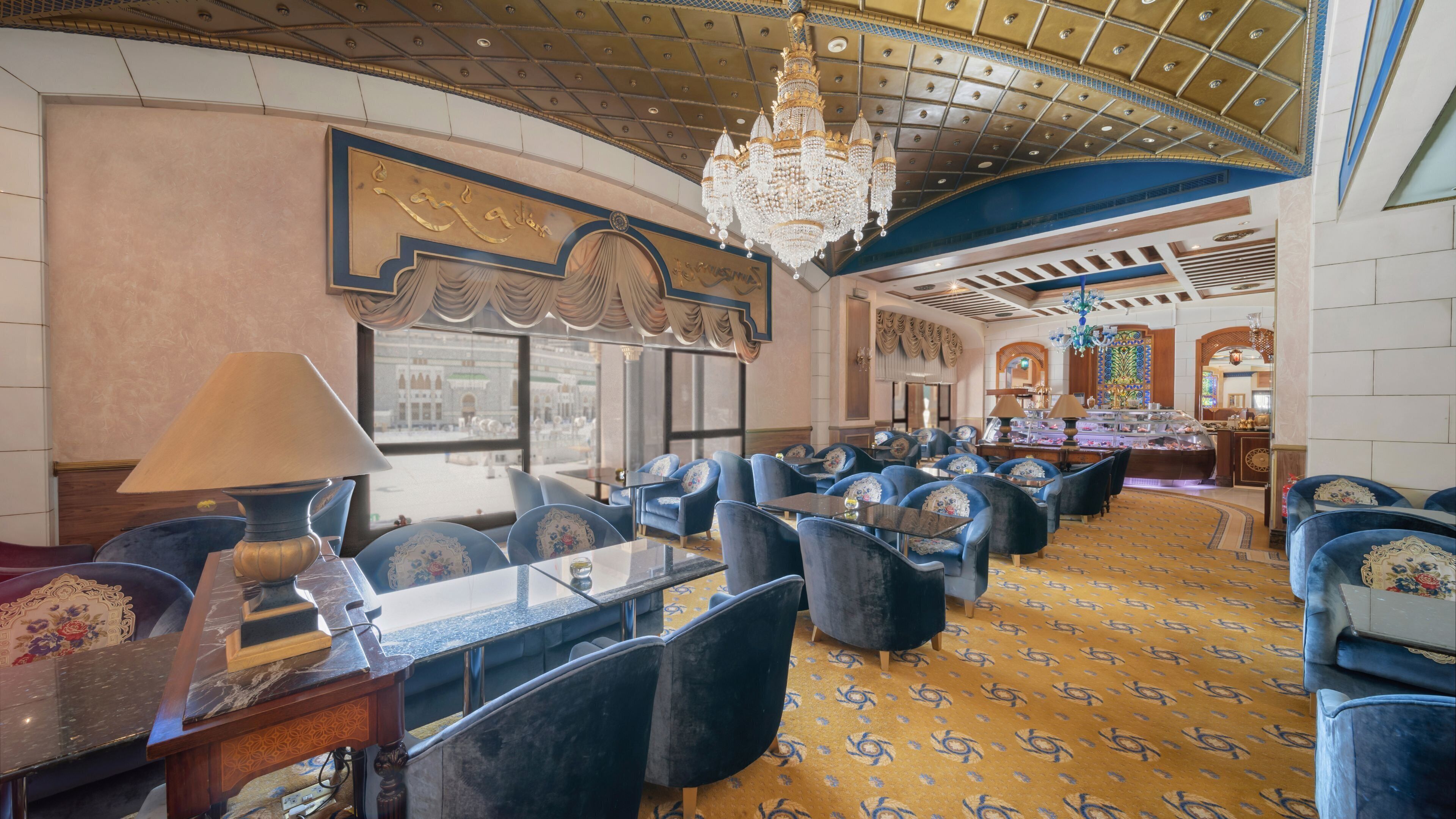 Eine geräumige Lobby mit einem gemusterten Teppich, blauen Polstersesseln und einer Kristallleuchter.