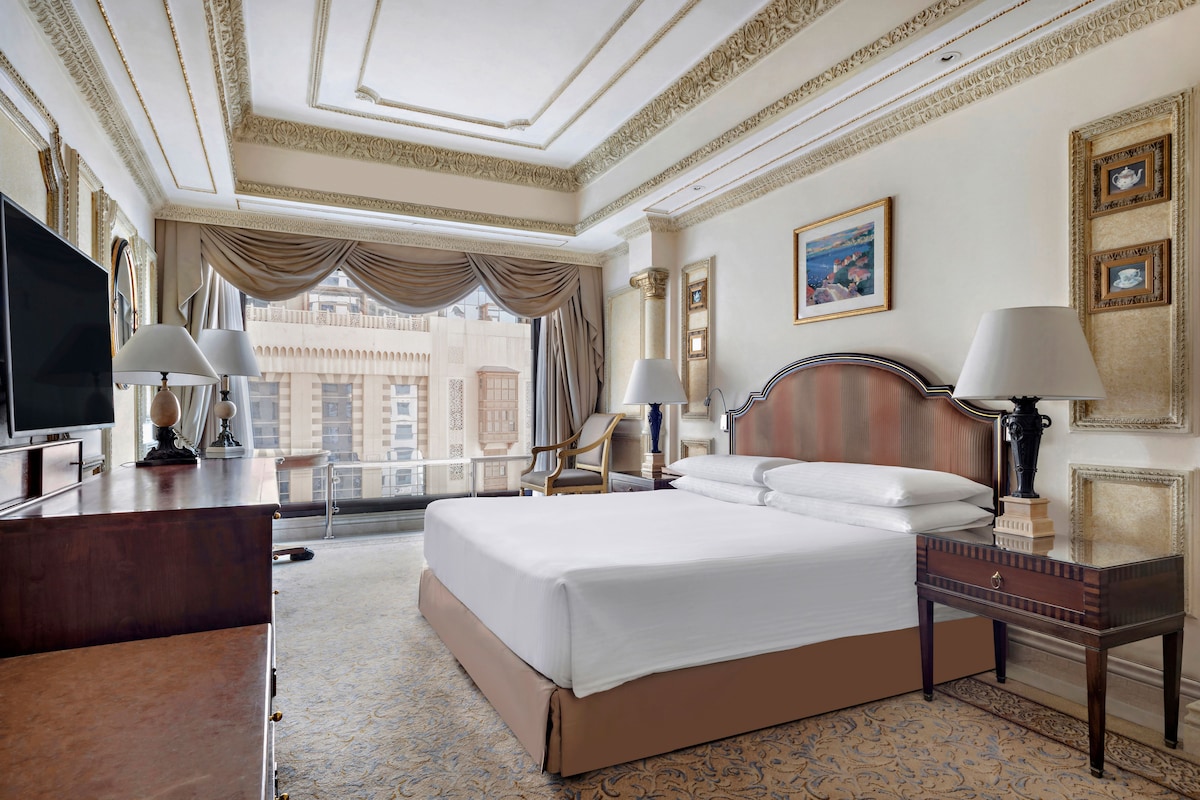 A hotel room with a large bed, a desk, a TV, and a view of the cityscape.