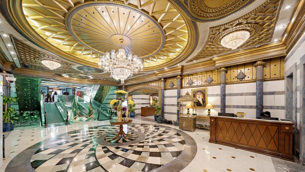 Un hall d'entrée luxueux, agrémenté d'un imposant lustre, d'un motif circulaire au centre du sol et d'un comptoir d'accueil.