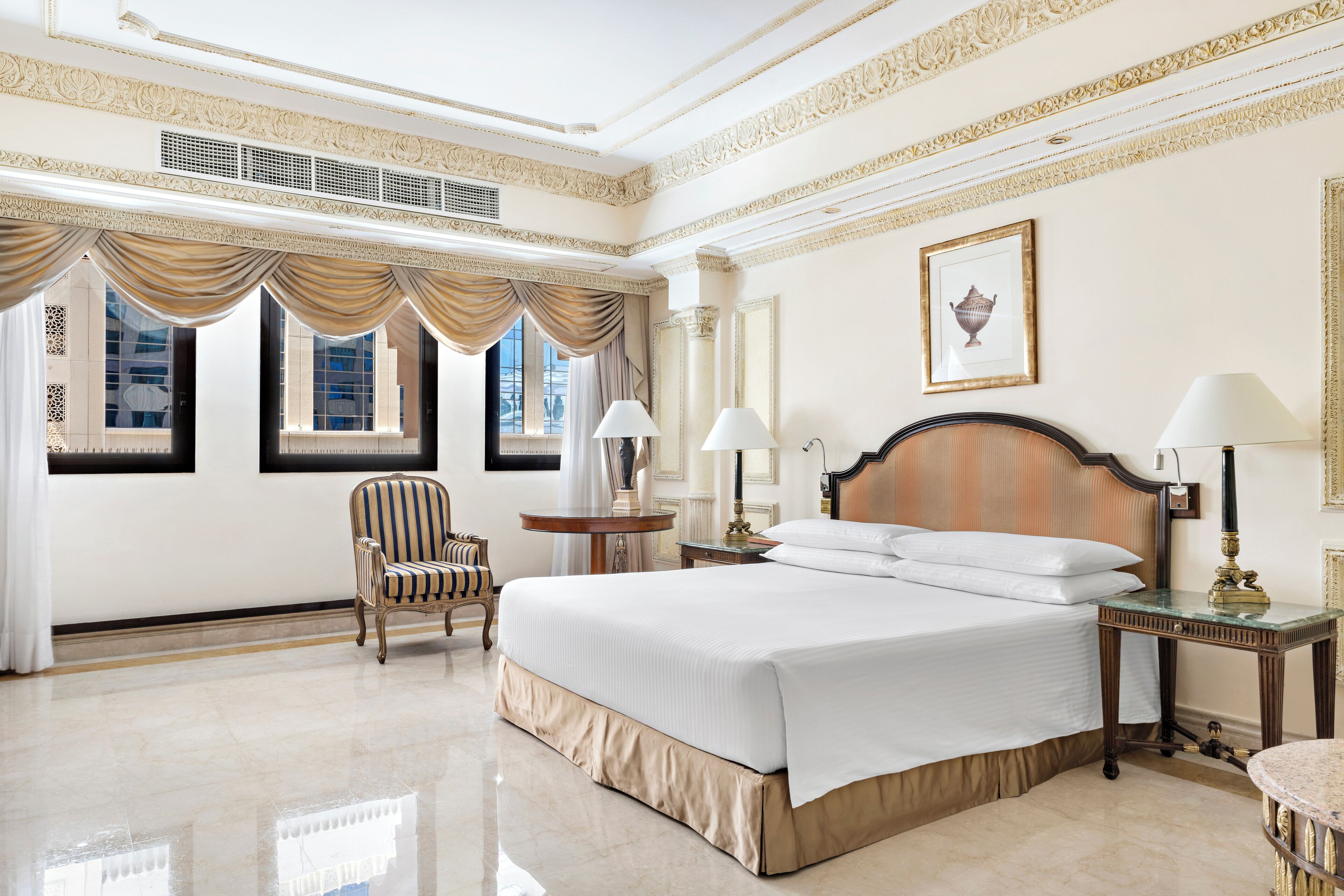 A spacious hotel room with a large bed, two bedside tables, a chair, and a window with curtains.